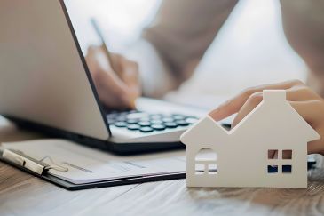 Foto: Person bearbeitet Akten, Modell eines Hauses im Vordergrund